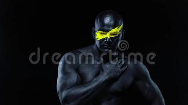 男子体育迷和健美运动员与黄色的脸艺术和黑色的身体油漆。 他的彩色画像